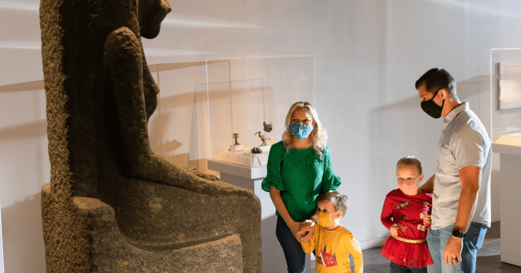 A family of four stands with masks on admiring an Egyptian statue at the San Antonio Museum of Art