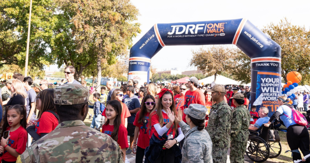 A large group of people are taking part in a JDRF One Walk and high fiving as they walk under a branded JDRF arch
