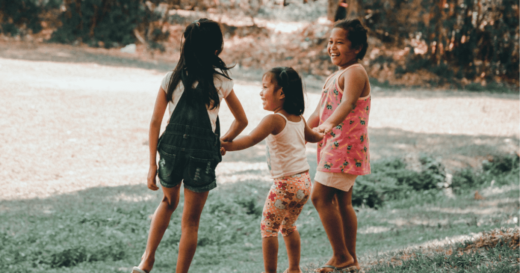An image of three young girls smiling and playing outside